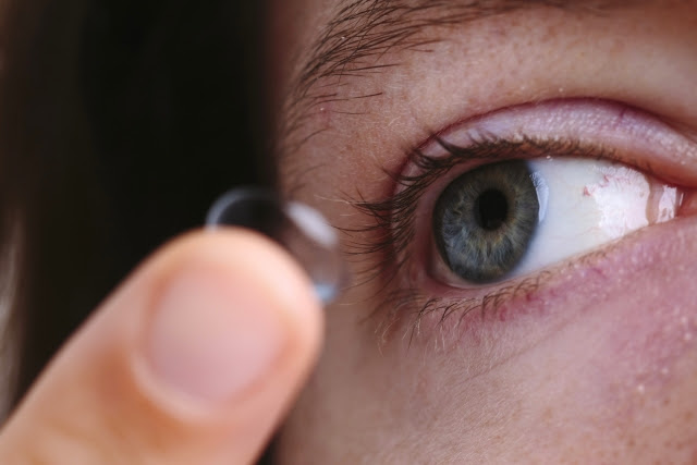 Close up of someone placing a contact into their right eye with their finger.